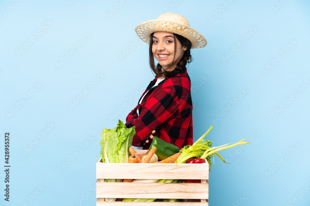 Young farmer Woman holding fresh vegetables in a wooden basket with arms crossed and looking forward