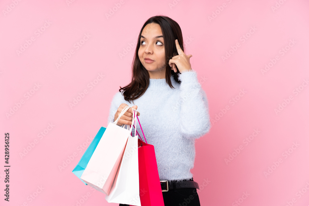 Young woman with shopping bag over isolated pink background having doubts and thinking