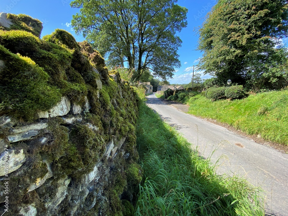 Country lane, with moss covered dry stone walls, leading down into the village of, Rylstone, Skipton, UK