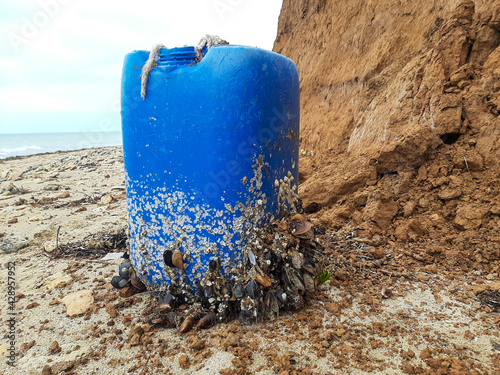 A plastic canister overgrown with shells on the seashore.