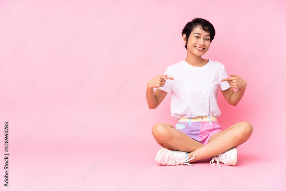 Young Vietnamese woman with short hair sitting on the floor over isolated pink background proud and self-satisfied Young Vietnamese woman with short hair sitting on the floor over isolated pink background proud and self-satisfied