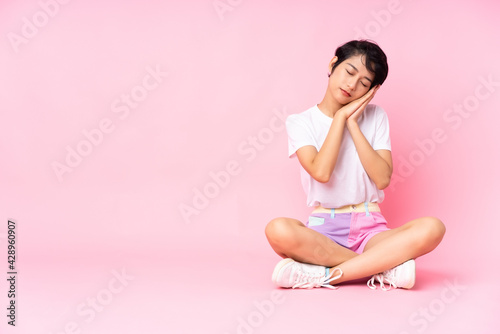 Young Vietnamese woman with short hair sitting on the floor over isolated pink background making sleep gesture in dorable expression