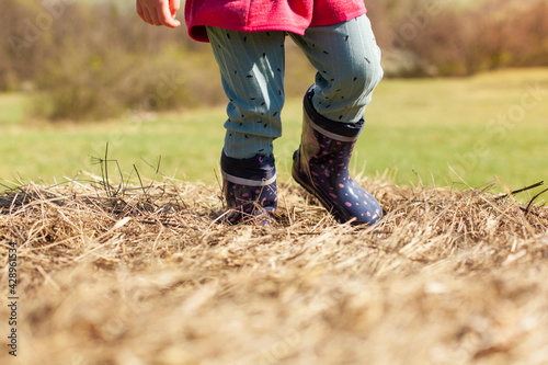 Child stands in the straw with rubber boots. Kind steht mit Gummistiefeln im Stroh.