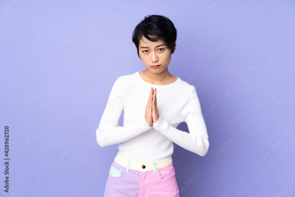 Young Vietnamese woman with short hair over isolated purple background keeps palm together. Person asks for something Young Vietnamese woman with short hair over isolated purple background keeps palm together. Person asks for something