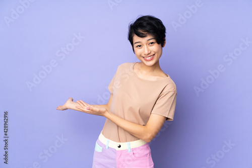 Young Vietnamese woman with short hair over isolated purple background extending hands to the side for inviting to come