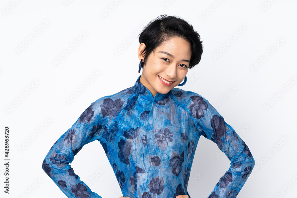 Young Vietnamese woman with short hair wearing a traditional dress over isolated white background posing with arms at hip and smiling Young Vietnamese woman with short hair wearing a traditional dress over isolated white background posing with arms at hip and smiling