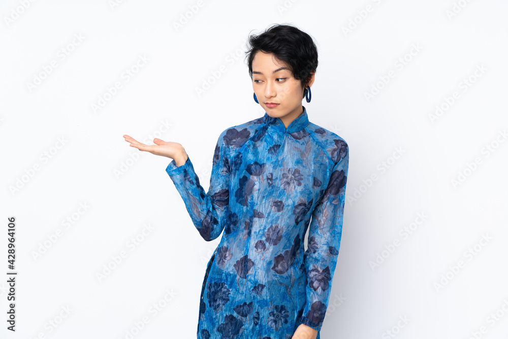 Young Vietnamese woman with short hair wearing a traditional dress over isolated white background holding copyspace with doubts Young Vietnamese woman with short hair wearing a traditional dress over isolated white background holding copyspace with doubts