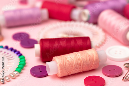 Sewing accessories including thread spools and pins on pink background