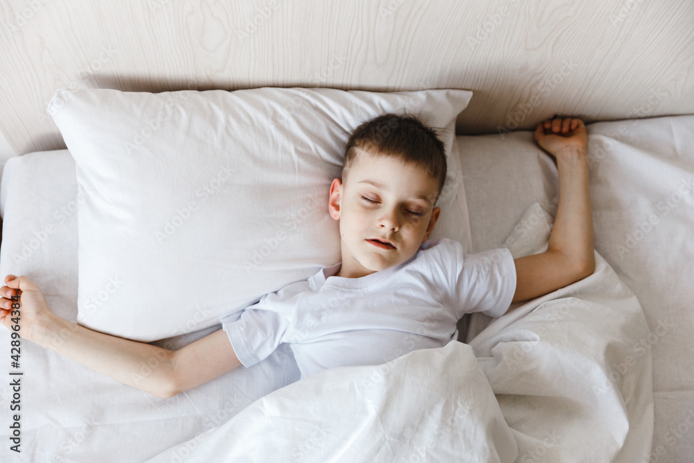 Cute little caucasian boy wake up in his comfortable bed in the morning under sun light. Stretches and yawns. Good morning Cute little caucasian boy wake up in his comfortable bed in the morning under sun light. Stretches and yawns. Good morning