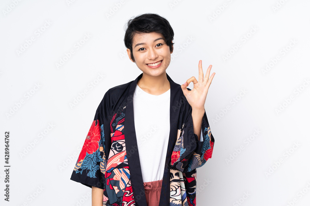 Young Vietnamese woman with short hair wearing a traditional dress over isolated white background showing ok sign with fingers Young Vietnamese woman with short hair wearing a traditional dress over isolated white background showing ok sign with fingers