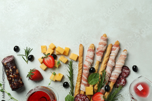 Grissini sticks with bacon, snacks and wine on white textured background