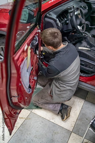 Mechanic guy in automobile service stay on a knees near car door at time of it dismantling to repair car after road accident