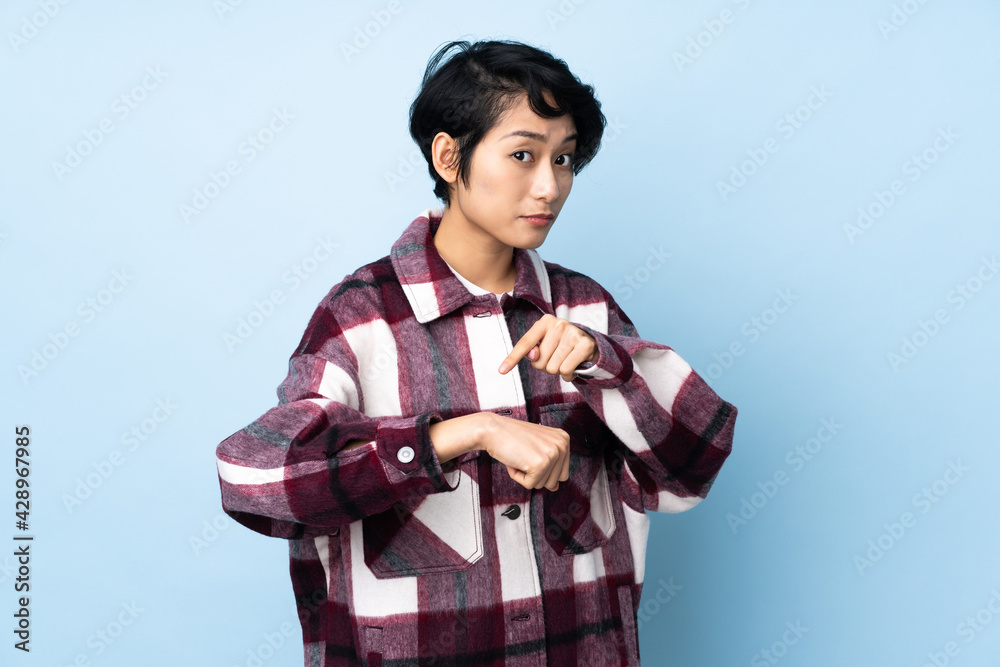 Young Vietnamese woman with short hair over isolated background making the gesture of being late Young Vietnamese woman with short hair over isolated background making the gesture of being late