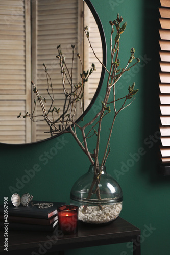 Beautiful tree twigs in vase on table near green wall
