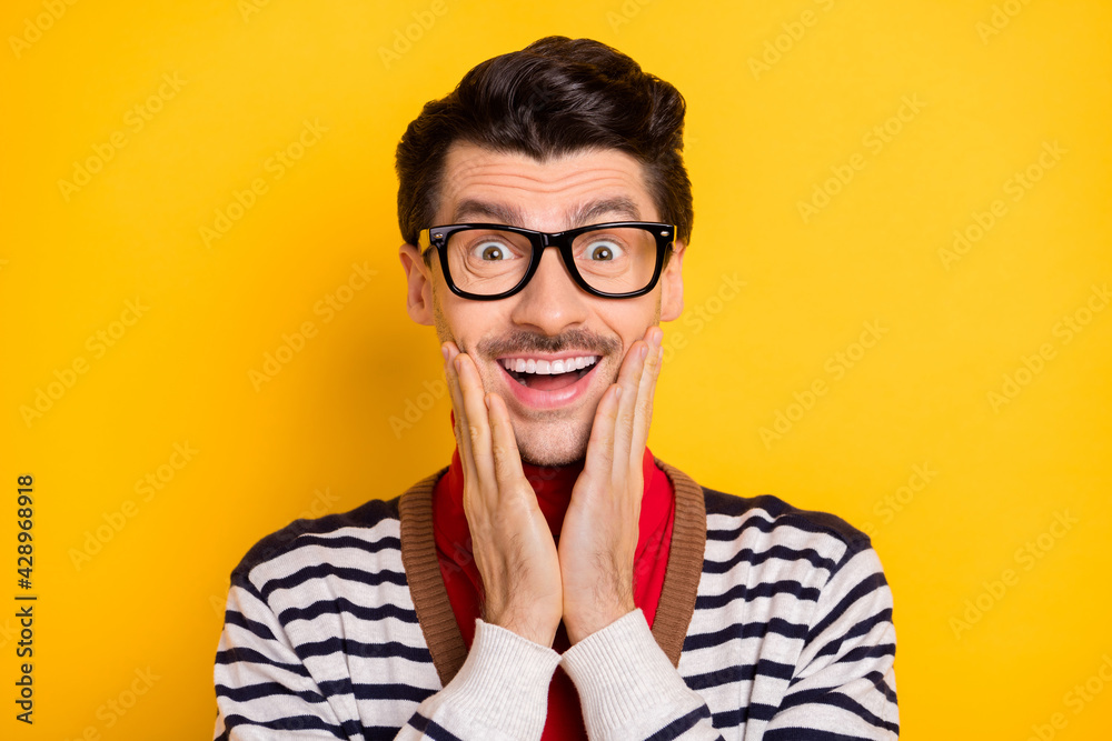 Photo of young man happy positive smile amazed shocked surprised news sale hands touch cheeks isolated over yellow color background Photo of young man happy positive smile amazed shocked surprised news sale hands touch cheeks isolated over yellow color background