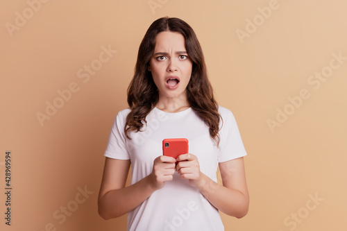 Photo of unhappy frustrated cute lady hold phone open mouth posing on beige background