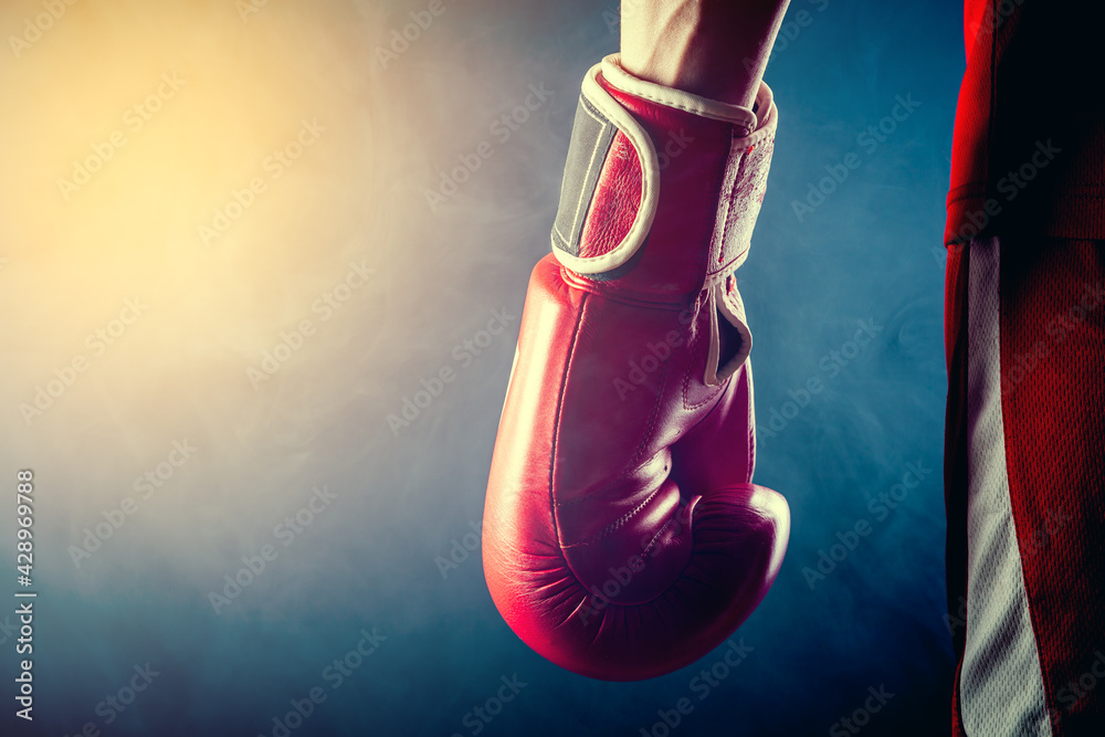 The hand of an athlete in a boxing glove on a dark background.