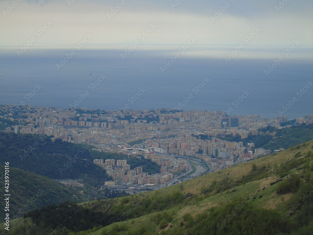 Genova, Italy - April 14, 2021: Panoramic view to the mountains over the city of Genova, and small part of the port. Grey sky in the background.