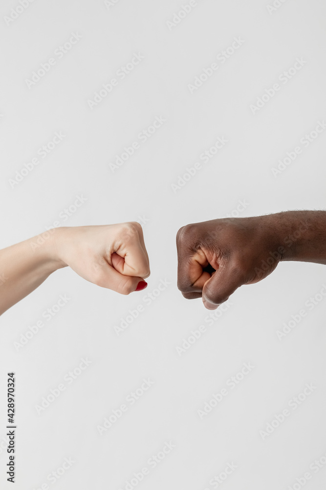 Multiethnic tolerance. Gender diversity. Racial cooperation. Discrimination problem. Conceptual art. White female and black male fists going to join together isolated light. Multiethnic tolerance. Gender diversity. Racial cooperation. Discrimination problem. Conceptual art. White female and black male fists going to join together isolated light.