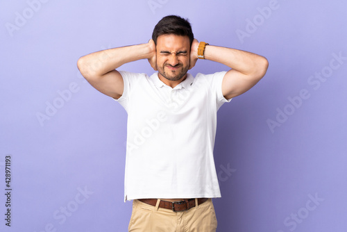 Young handsome man isolated on purple background frustrated and covering ears