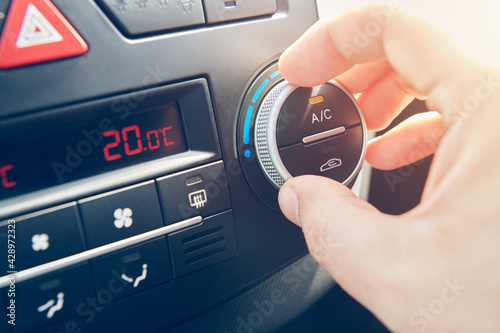 Man hand set the temperature of air conditioner in the car. Driver turning on car climate control system. travel by car. Close up view with selective focus.
