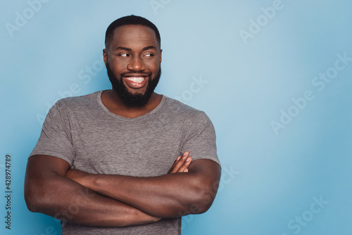 Positive dark skin guy hold arms crossed look empty space isolated blue background