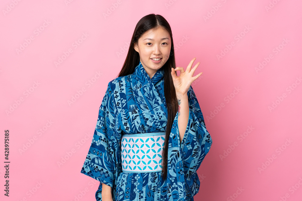 Young Chinese girl wearing kimono over isolated background showing ok sign with fingers Young Chinese girl wearing kimono over isolated background showing ok sign with fingers