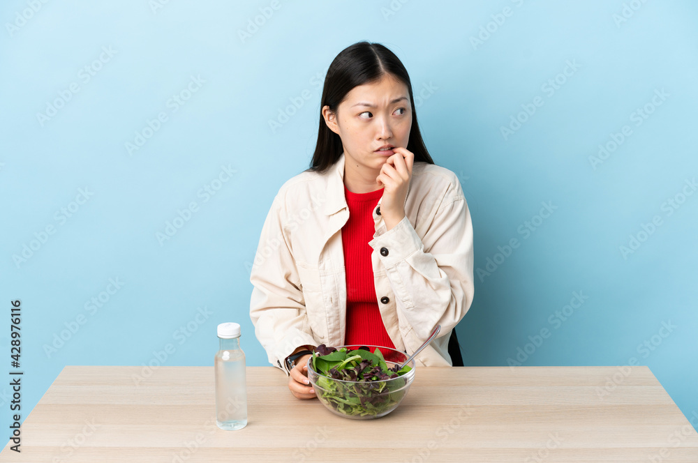 Young Chinese girl eating a salad nervous and scared Young Chinese girl eating a salad nervous and scared