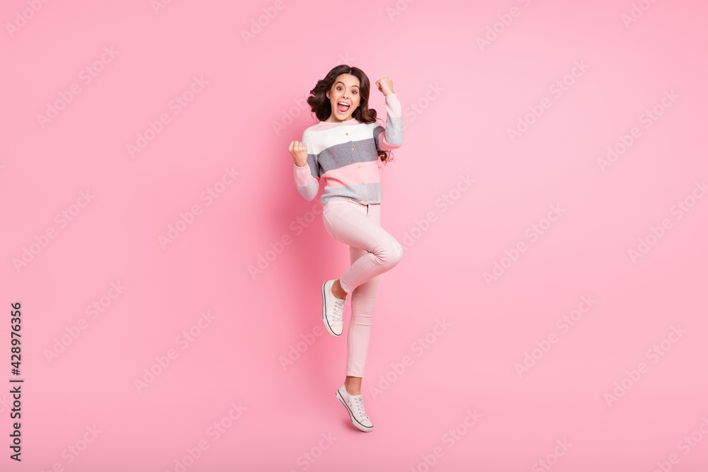 Full body photo of attractive small girl kid jump up raise fists celebrate win isolated on pink color background