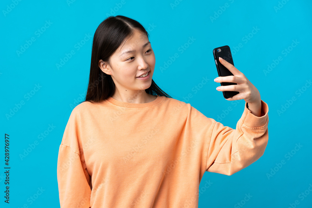 Young Chinese girl over isolated blue background making a selfie Young Chinese girl over isolated blue background making a selfie