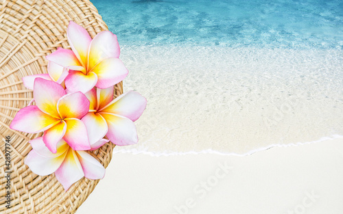 Colorful Plumeria flower on rattan tray over white beach background, summer concept, outdoor day light