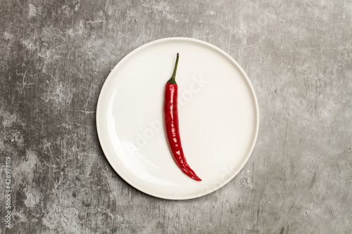 Un pimiento rojo chili sobre un plato redondo en un fondo con textura gris aislado. Vista superior. Copy space