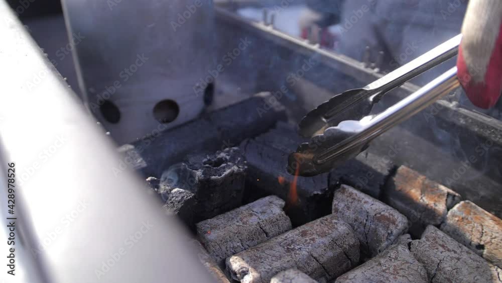 Stirring coals in the grill. The rounded coconut charcoal is smoldering. Grilling coals. Organizational preparation for barbecue grilling. Basis for frying trdylnik. Street food. Stirring coals in the grill. The rounded coconut charcoal is smoldering. Grilling coals. Organizational preparation for barbecue grilling. Basis for frying trdylnik. Street food.