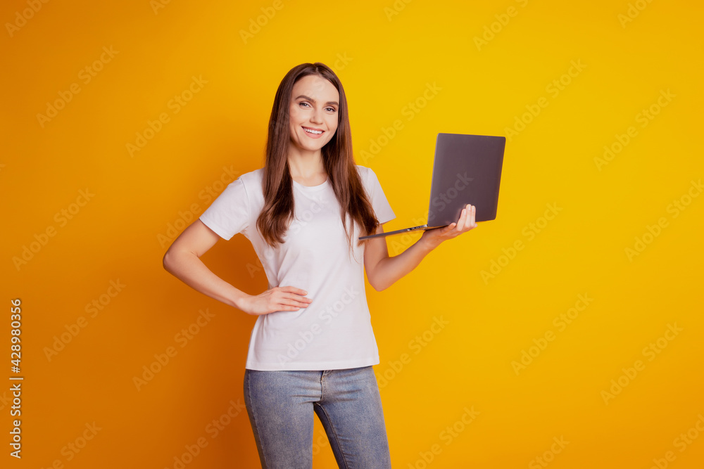 Photo of programmer lady hold netbook beaming smile wear white t-shirt posing on yellow background Photo of programmer lady hold netbook beaming smile wear white t-shirt posing on yellow background