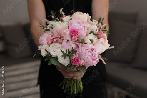 Pink wedding bouquet, composed of roses, freesias, peonies, hypericum, astilba and eucalypthus, in florist hands.
