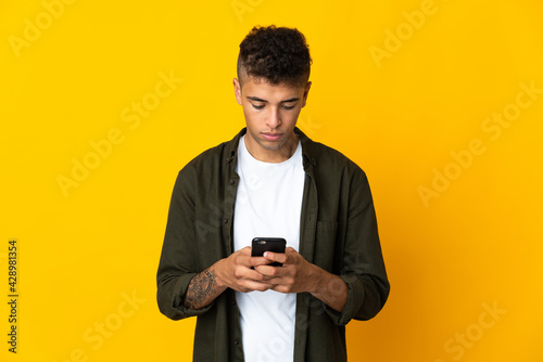 Young brazilian man isolated on yellow background using mobile phone