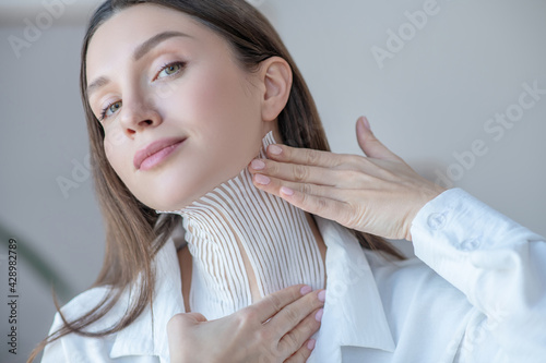 Cute young woman putting tapes on her neck and looking contented photo