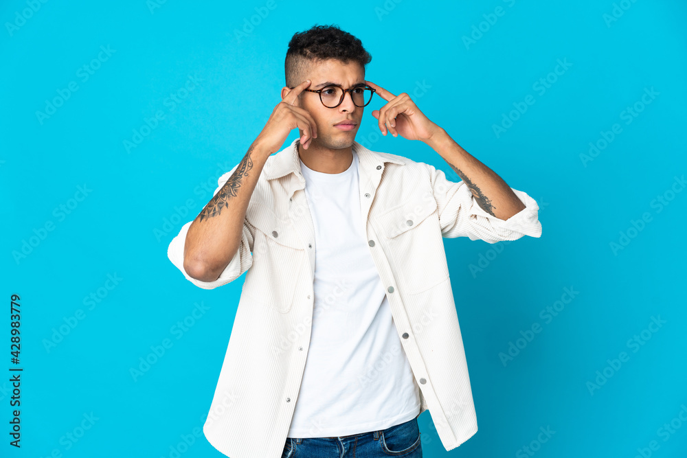 Young Brazilian man isolated on blue background having doubts and thinking