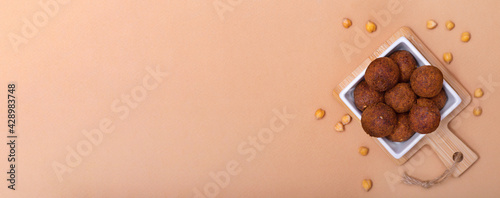 Horizontal banner with fried falafel in square bowl and chickpea on beige background. Healthy roasted vegetarian fastfood. Jewish cuisine. Copy space.