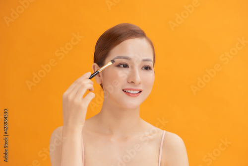 Beautiful woman using brush for eyeshadow. Photo of woman with perfect makeup on yellow background. Beauty concept