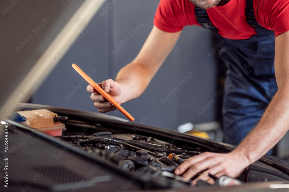 Male hands with tablet under hood of car