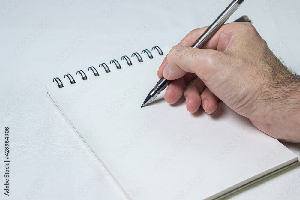Blank notepad sheet, background for lettering and logo. A hand holds a pen by a sheet of notepad Blank notepad sheet, background for lettering and logo. A hand holds a pen by a sheet of notepad