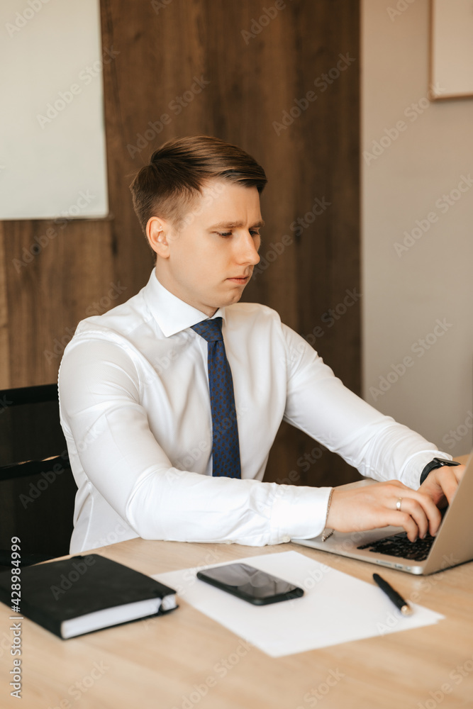 Fototapeta premium Young male businessman working on laptop in office