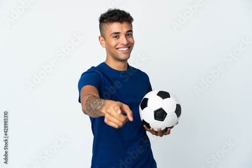 Young Brazilian man over isolated background with soccer ball and pointing to the front © luismolinero