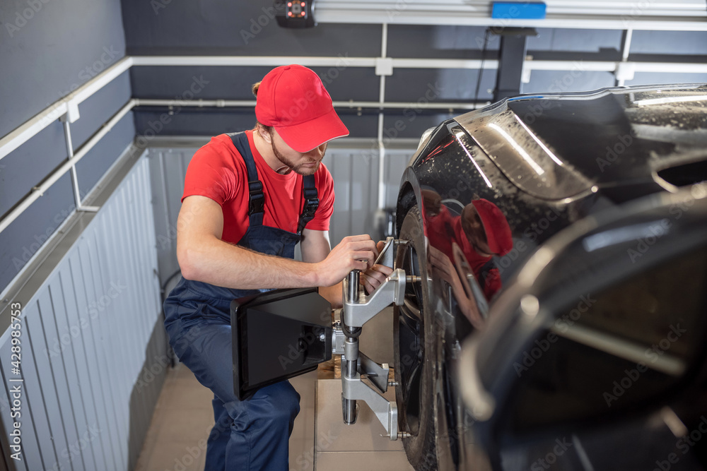 Auto mechanic in overalls near wheel of car