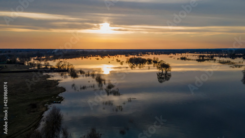 Aerial view of the setting sun beautifully illuminates cumulus clouds slowly floating over a full-flowing river on a warm spring evening. Sunset panorama over the river. Travel and journey concept. © kalyanby