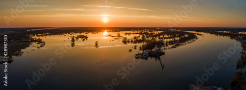 Aerial view of the setting sun beautifully illuminates cumulus clouds slowly floating over a full-flowing river on a warm spring evening. Sunset panorama over the river. Travel and journey concept.