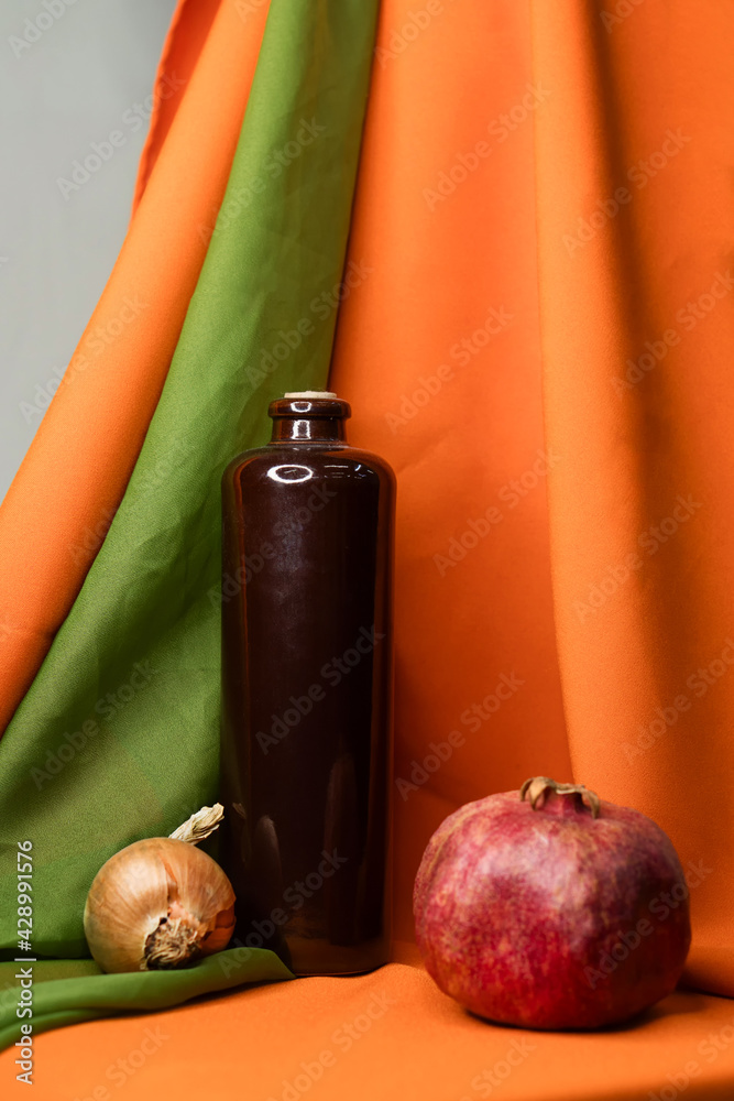 Educational still life for drawing. Dark glass bottle, pomegranate and onion on a bright cloth background