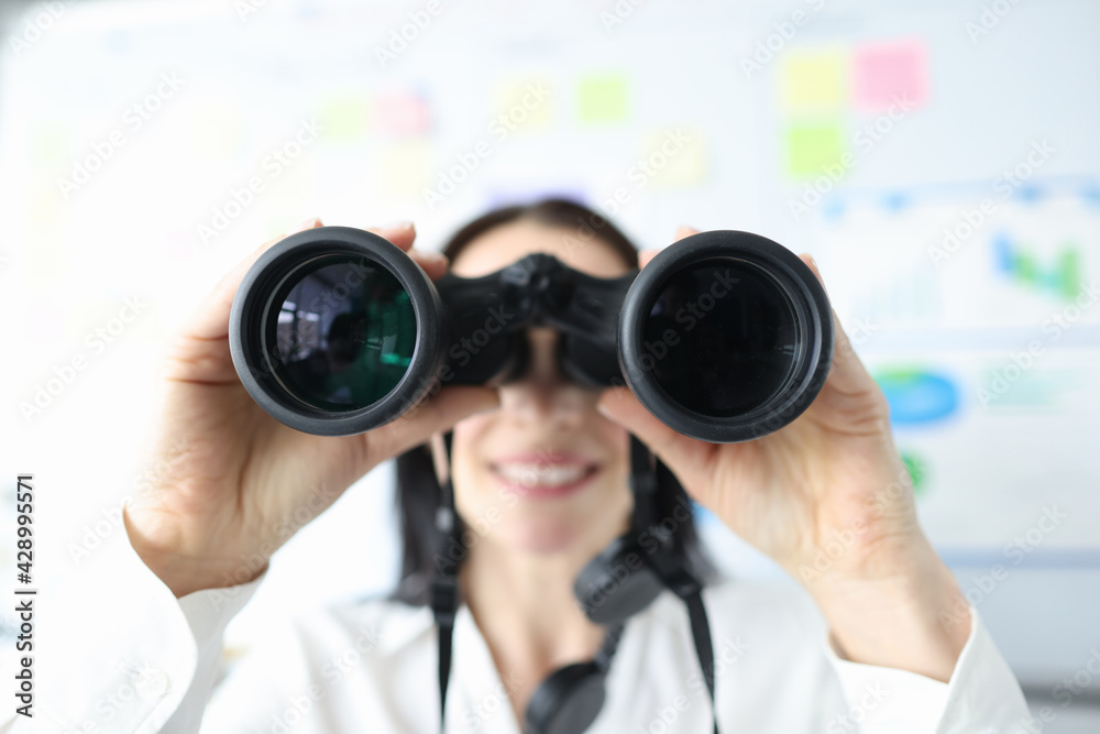 Woman looking through black binoculars in office closeup Woman looking through black binoculars in office closeup