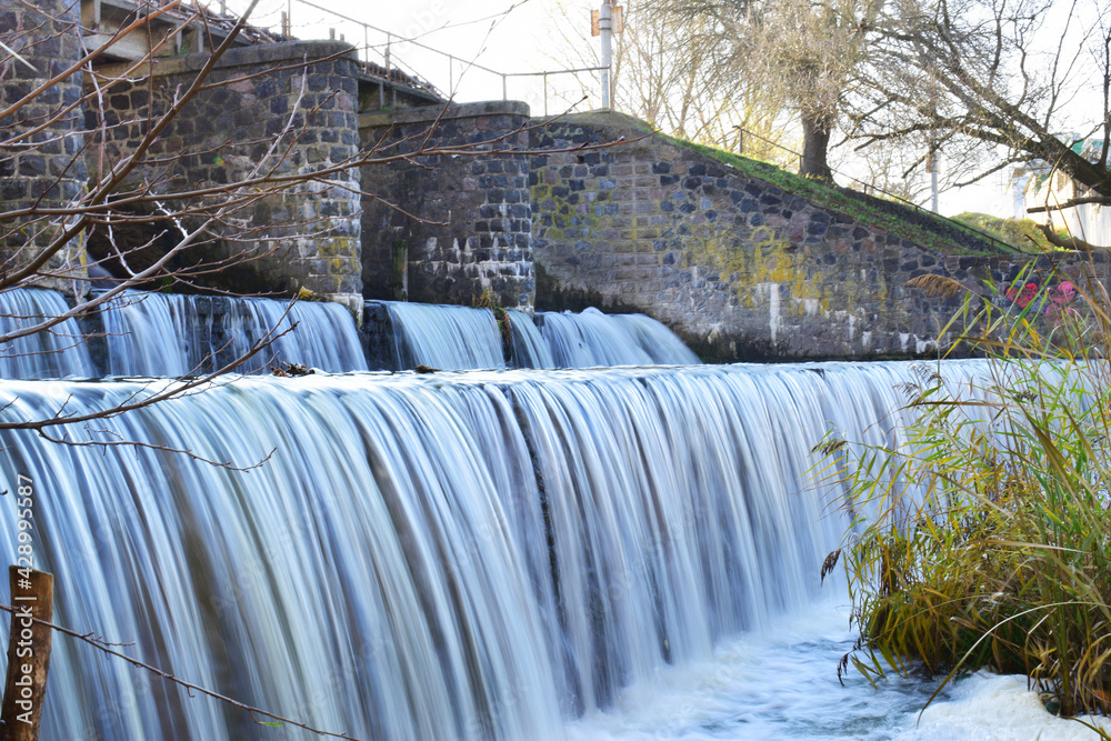 Naklejka premium river dam. water release, The excess capacity of the dam until spring-way overflows. streams of water, stone walls, a large construction of a dam on a reservoir. water being released from a dam.